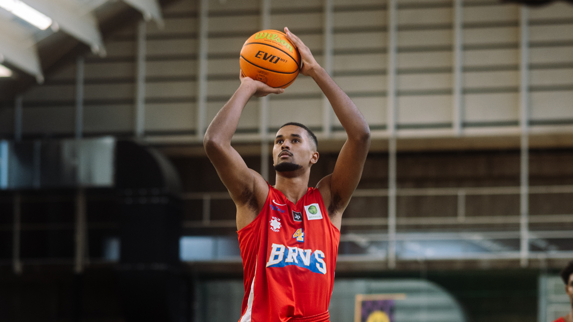 Photo: A Berlin Braves player holds a basketball between his raised arms. 