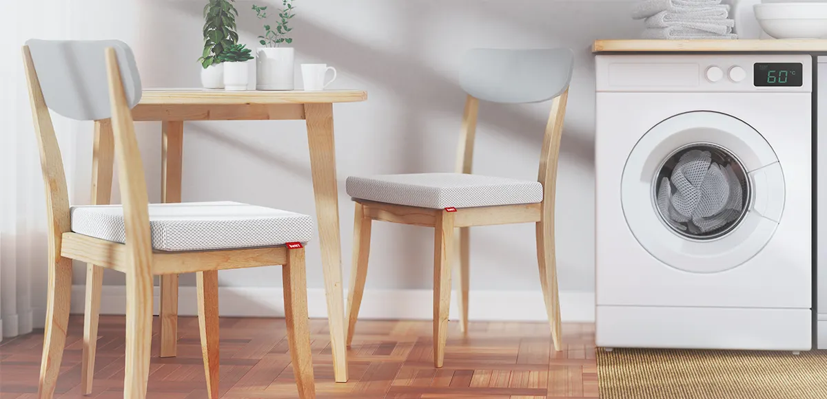 A table with two chairs on which the BODYGUARD® seat cushion is placed. Next to it is a washing machine.