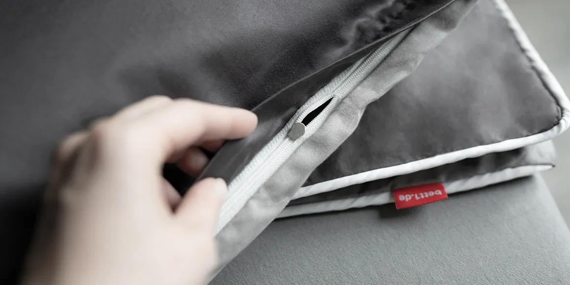 Photo: A hand holds the folded SOFT BREEZE satin bed linen so that the zipper is visible.