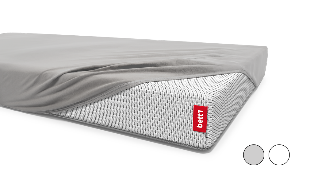 A children's mattress is covered with a fitted sheet except for one corner.