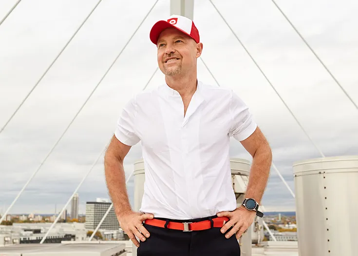 Photo: bett1.de Founder Adam Szpyt stands on a rooftop with his hands on his hips, gazing into the distance. A city can be seen in the background.
