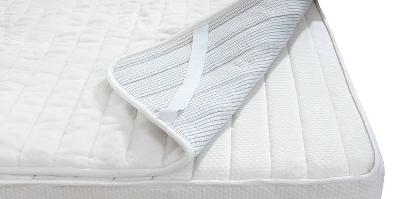 A thin mattress protector on a light-colored mattress. One corner is folded back, revealing the plastic underside.