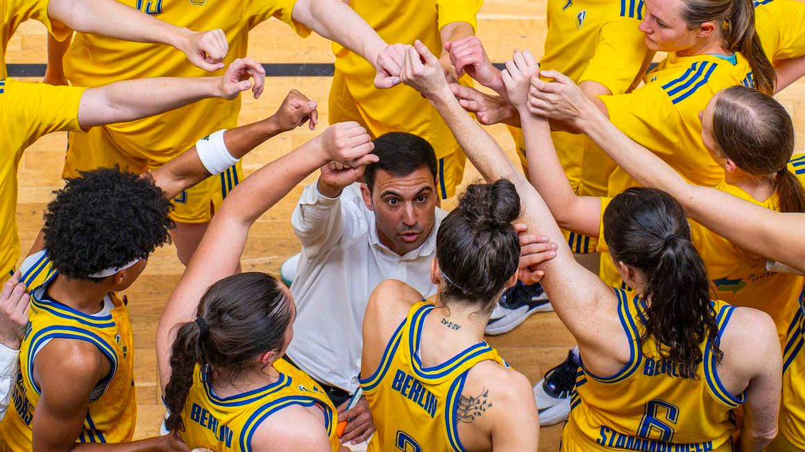 Photo from a bird's eye view: A person in a white shirt surrounded by people in yellow jerseys who put their hands over each other in the middle.