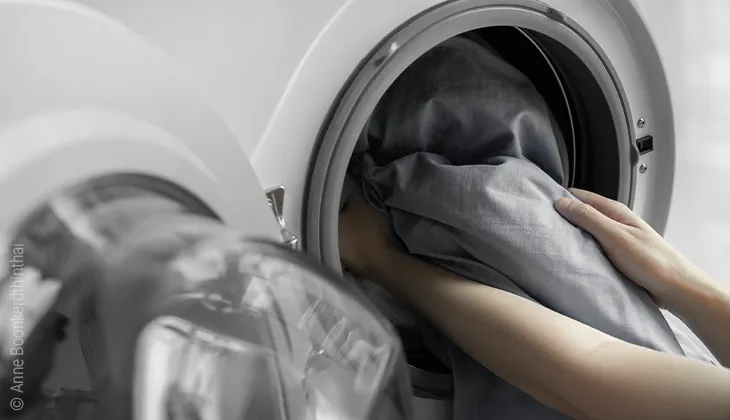 Photo: Hands holding bed linen reach into an open washing machine.