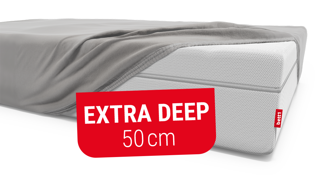 A high mattress is covered with a fitted sheet except for one corner. Text: extra deep 50 cm