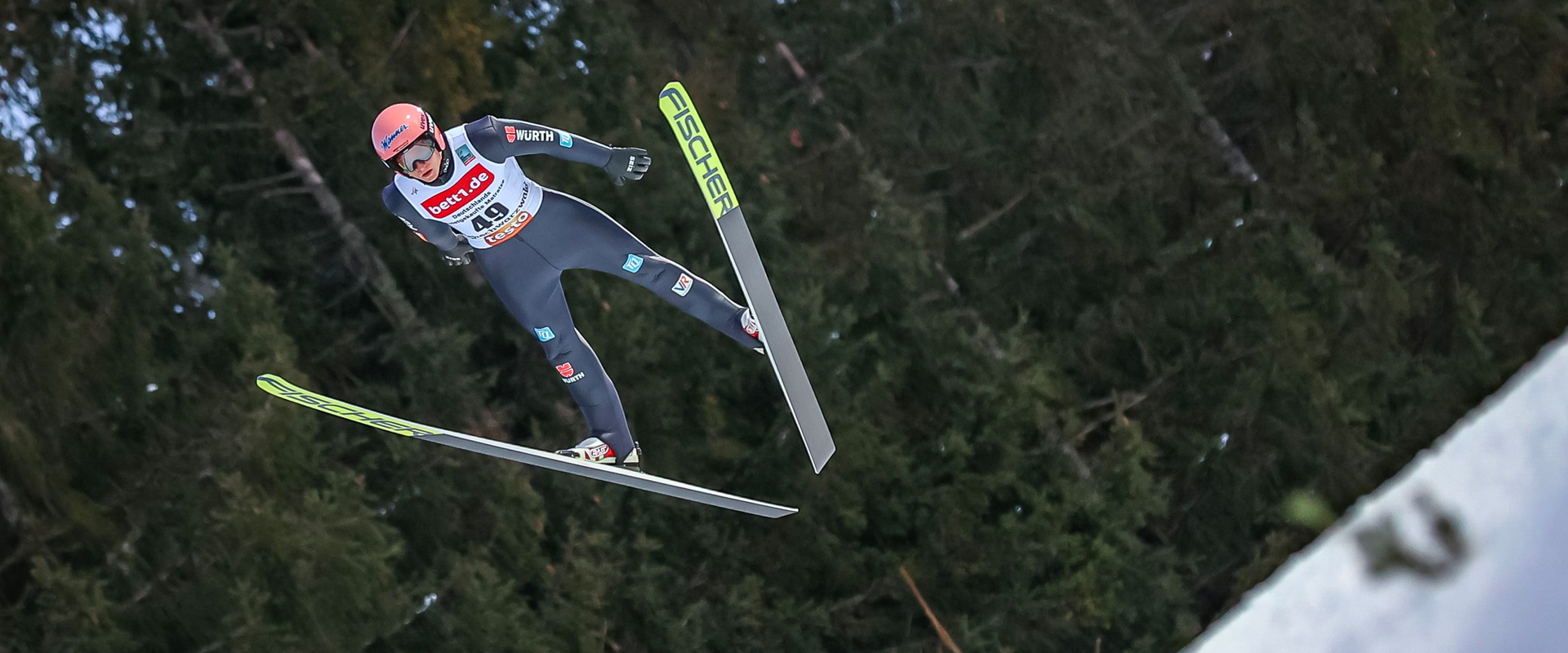 Photo: A person with skis in a jumping pose above a snowy forest.