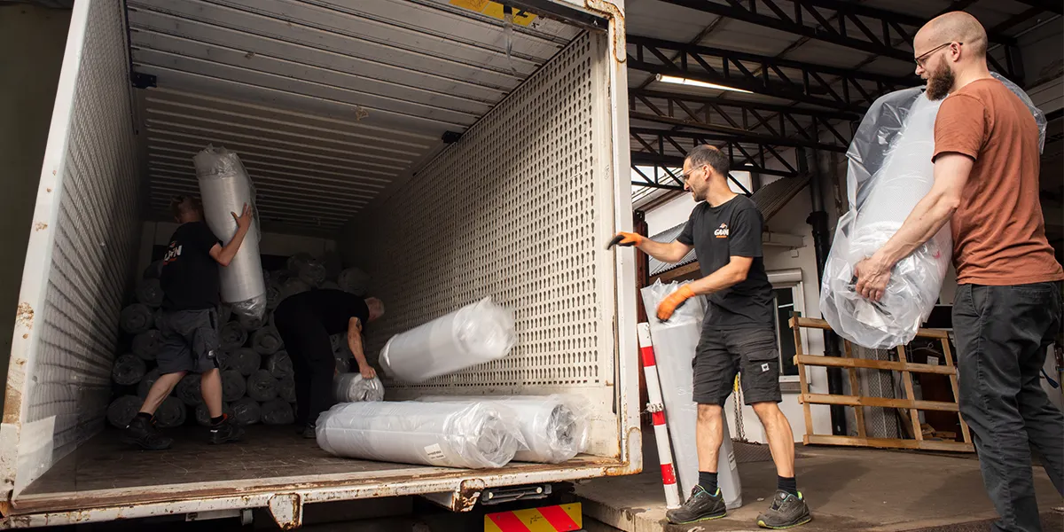 Foto: Drei Personen beladen einen Container mit zusammengerollten BODYGUARD Matratzen. 