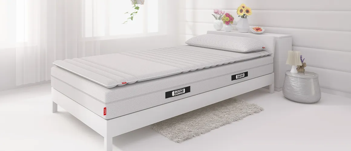 In einem hellen Schlafzimmer steht ein Bett 90x200 cm, darauf eine Matratze und ein Topper 90x200 cm und das Visko-Kissen.