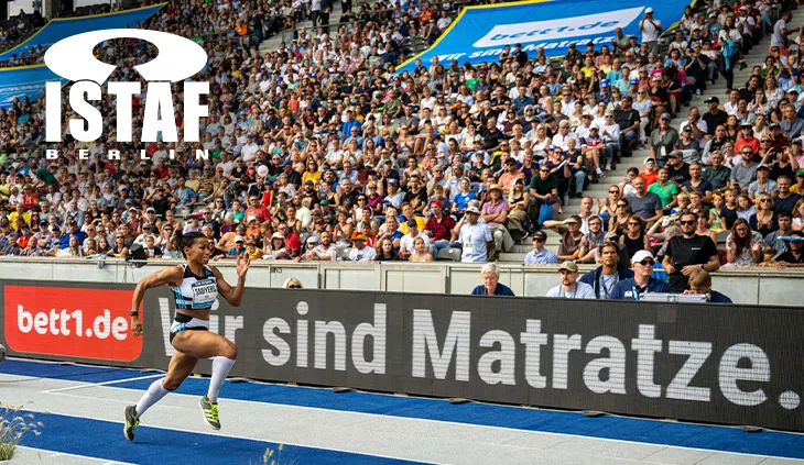 Foto von der ISTAF Berlin: Eine Person im Sprint vor einer vollen Tribüne. Auf der Bande das bett1.de Sponsoren-Logo. 