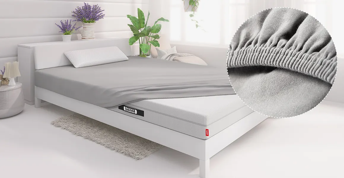 A BODYGUARD mattress lies in a bed in a bedroom, covered with a 140x200 cm fitted sheet. A circular cutout shows a close-up of the elastic band.