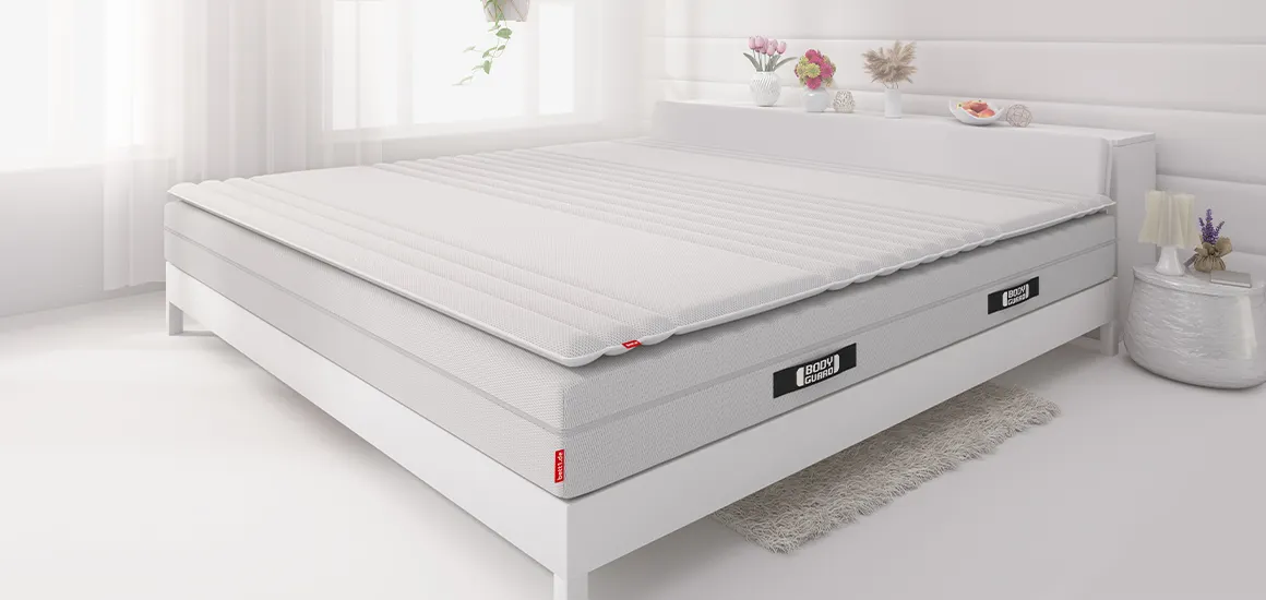 The BODYGUARD® mattress lies in a bed with the BODYGUARD® Topper on top.
