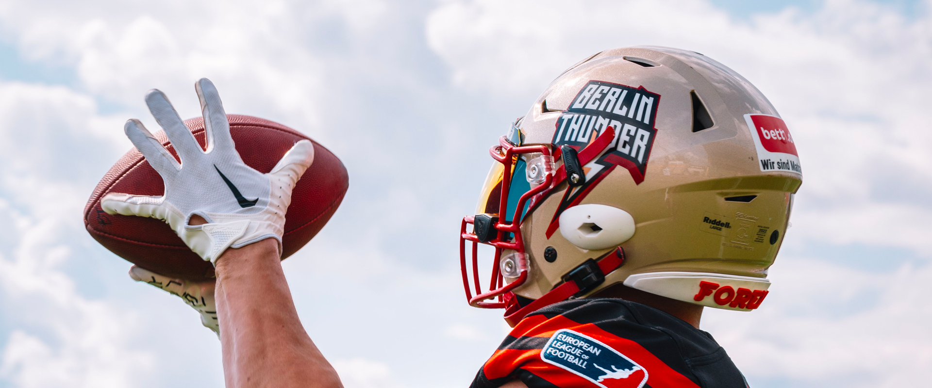 Photo: A person with a football helmet and football in his hands from behind.