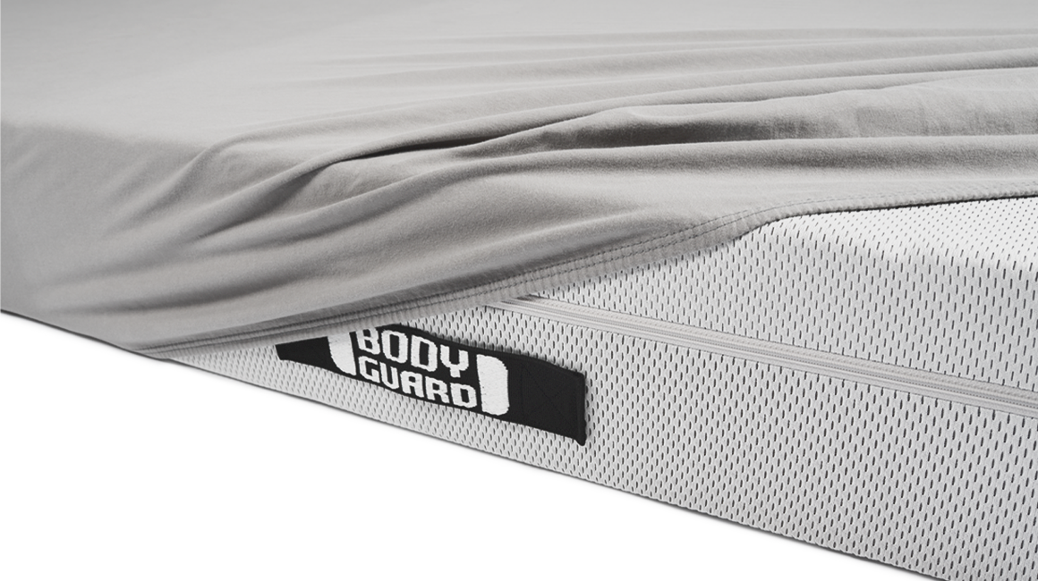 The BODYGUARD jersey fitted sheet lies half-unfolded on a bett1 mattress