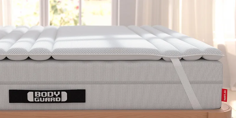 BODYGUARD mattress with a BODYGUARD topper on a wooden bed in a bright bedroom.