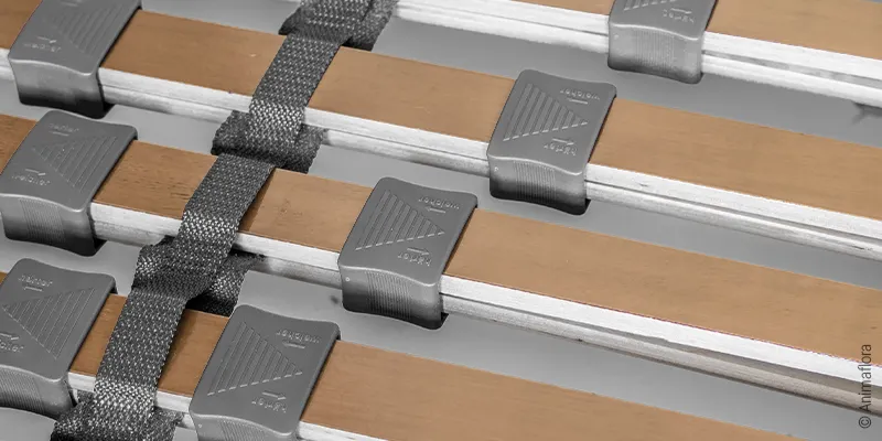 Close-up of the spring slats of a slatted frame with hardness settings: Two spring slats lying on top of each other are enclosed by an adjustment slider.