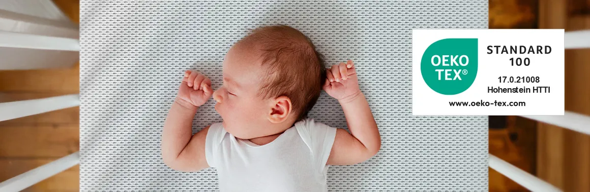 Photo taken from above: A baby sleeping on the BODYGUARD baby mattress, with the Oeko-Tex label next to it.