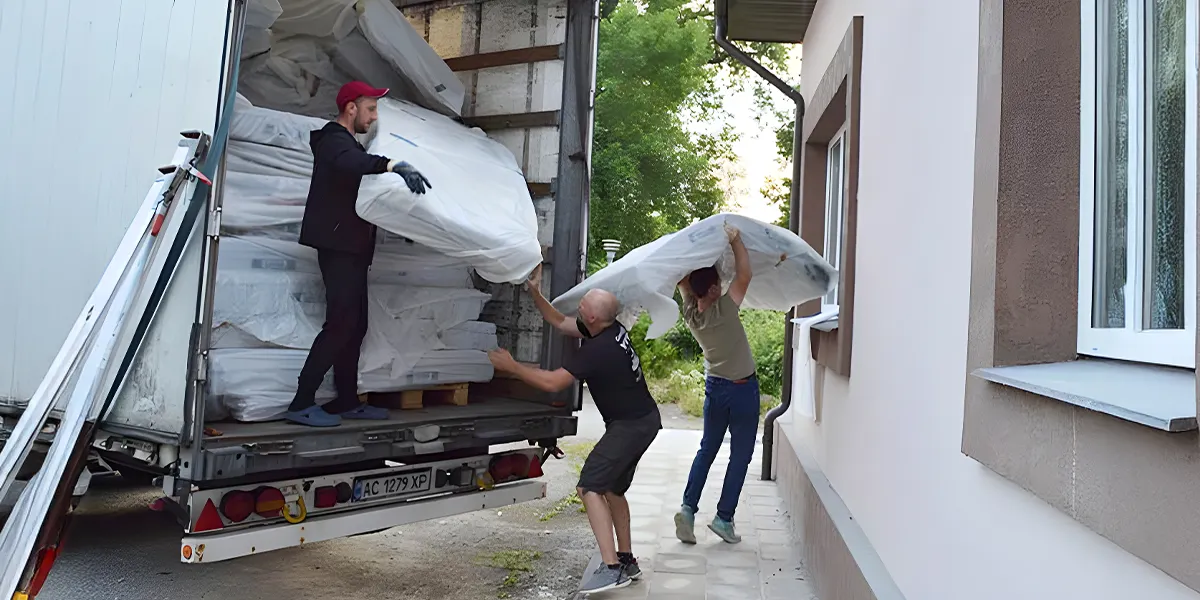 Foto: Drei Personen entladen einen Lkw mit gestapelten BODYGUARD Matratzen.