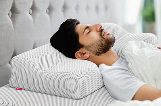 Photo: A person is lying on their back on the BODYGUARD neck support pillow in an upholstered bed.