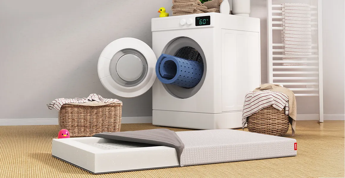 Die SuperBreeze Kindermatratze mit halb geöffnetem Bezug liegt vor einer Waschmaschine. Eine waschbare Liegefläche schaut zusammengerollt aus der Waschmaschine.