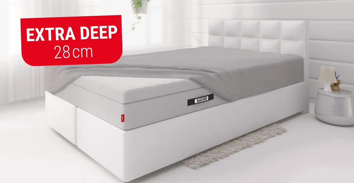The BODYGUARD box spring mattress lies in a bed and is covered with the extra-high BODYGUARD fitted sheet, except for one corner. A red box with text: extra deep 50 cm. 