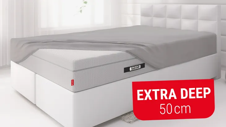 Photo: Bedroom with bed. The bed is fitted with the BODYGUARD box spring mattress, partially covered with the BODYGUARD Fitted Sheet 100 × 200 cm extra deep. Text: extra deep 50 cm