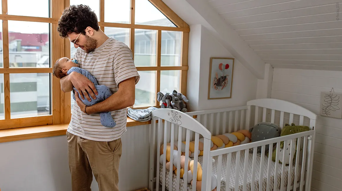 Photo: A person standing next to a crib, holding a baby in their arms.
