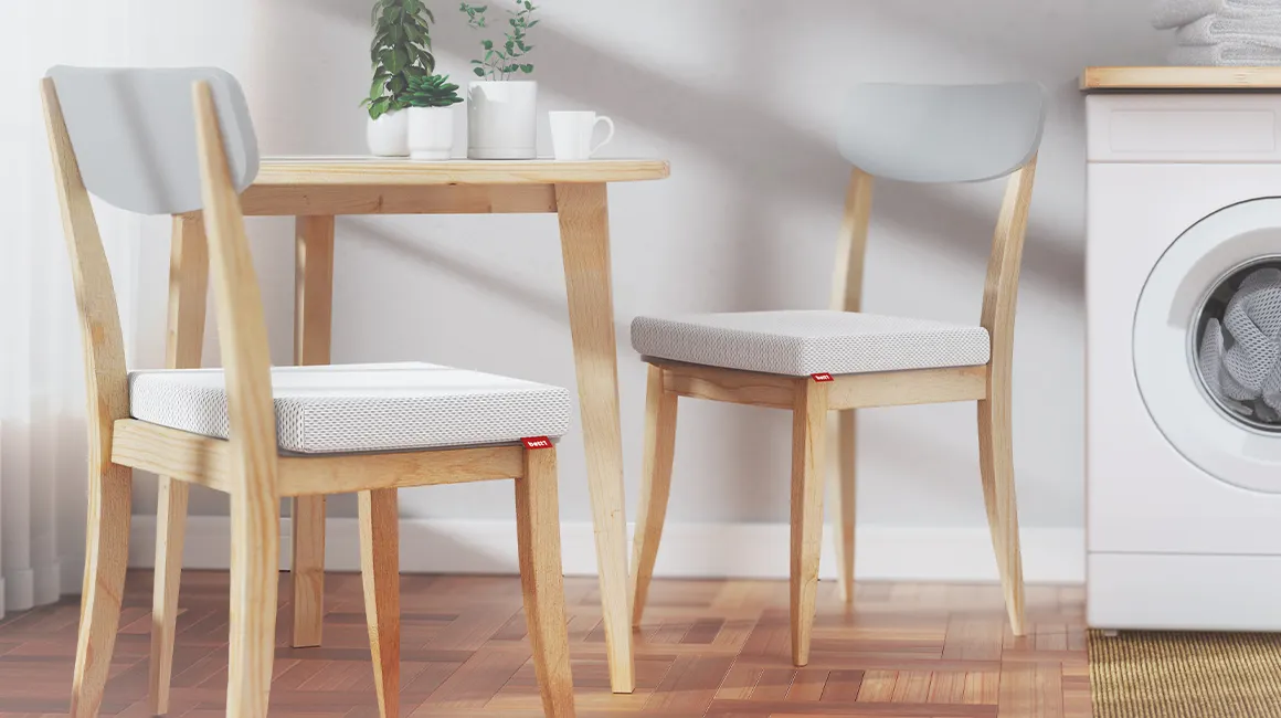 Two kitchen chairs stand at a kitchen table, on which the Bodyguard seat cushion 40x40 lies.
