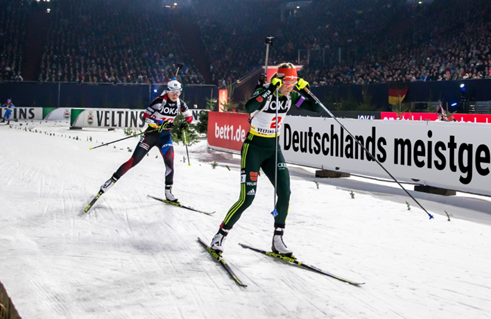 Photo: A few people on skis in a row on a running track in the stadium. The stadium banner reads in large letters: Germany's best-selling mattress.
