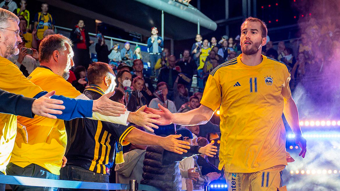 Photo: An ALBA Berlin player entering the hall, clapping off some hands extended towards him.