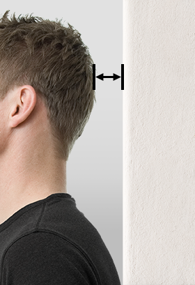 A person is standing with their back to the wall, and an arrow is drawn between the wall and the back of their head.