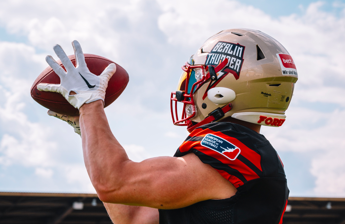 Photo: A person with football helmet and football in his hands from behind.