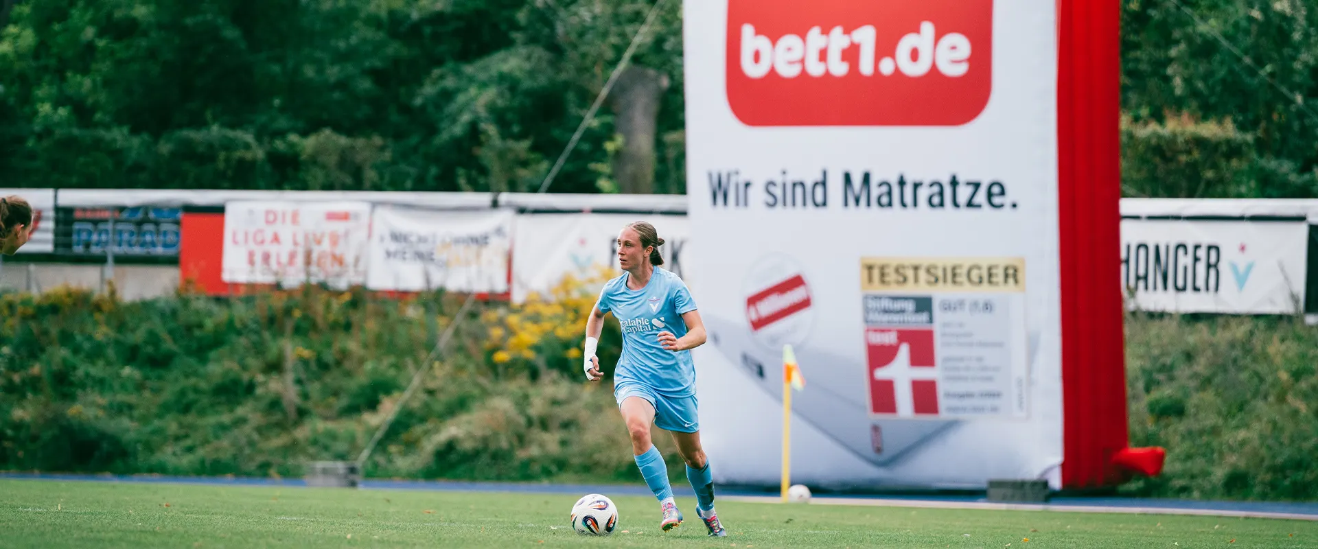 Foto: Spielerinnen mit unterschiedlichen Trikots auf einem Rasen.