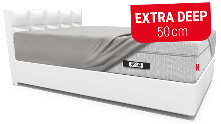 The BODYGUARD Box Spring Mattress, fitted with the extra-high BODYGUARD fitted sheet, lies on a light-coloured upholstered bed. Text: Extra Deep 50 cm.