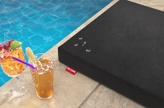 The RAINGUARD Seat Cushion lies on the edge of the pool with individual water droplets on its surface. Next to it are chilled drinks. 