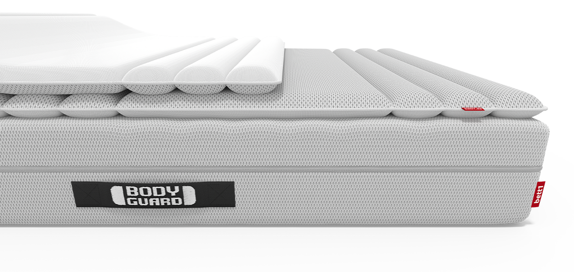 Eine BODYGUARD® Matratze halb bezogen mit dem BODYGUARD® Topper. Eine Topper-Hälfte ist umgeklappt und gibt die Sicht auf die zweite Bezugsseite frei. 