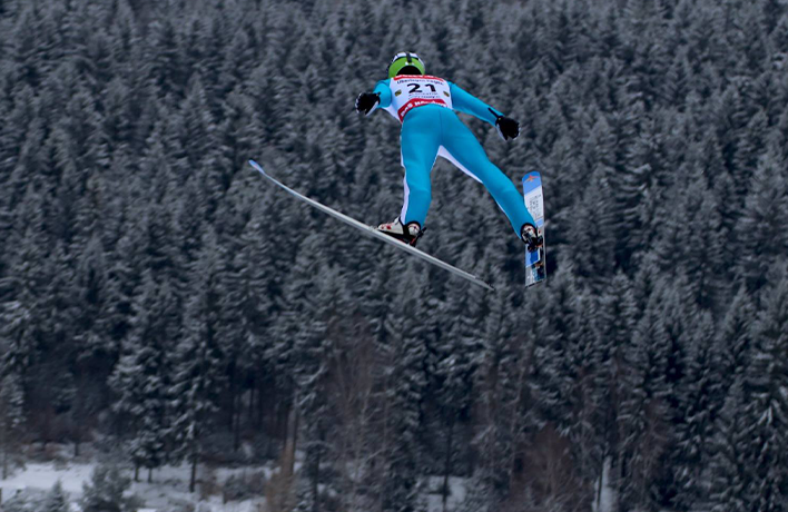 Photo: A person with skis in a jumping pose above a snowy forest.