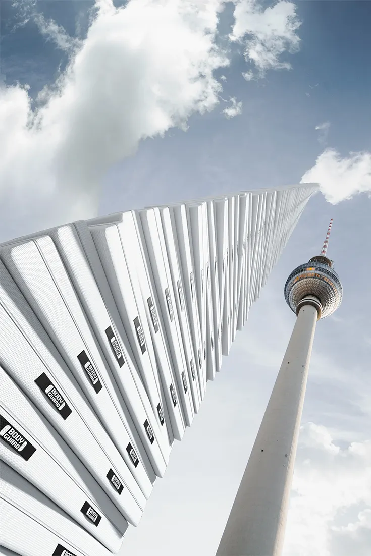 Ein Turm aus BODYGUARD Matratzen ragt in den Himmel. Daneben der Berliner Fernsehturm.