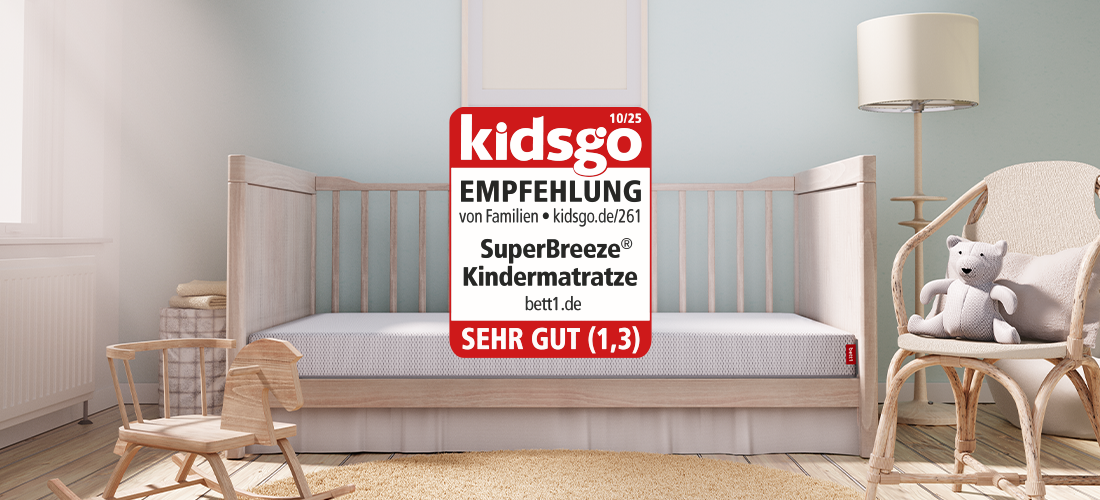 In einem Kinderzimmer steht ein nach vorne offenes Gitterbett, in dem die SuperBreeze Kindermatratze liegt, daneben das kidsgo-Siegel.