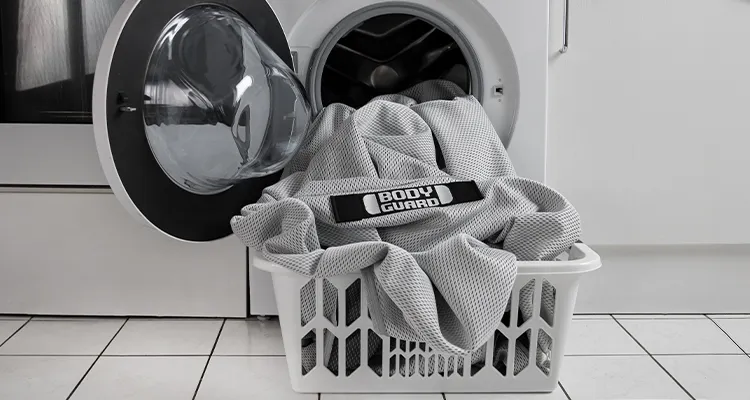 Foto: Vor einer geöffneten Waschmaschine steht ein Wäschekorb. Der HyBreeze Matratzenbezug steckt halb in der Maschine, halb im Korb.