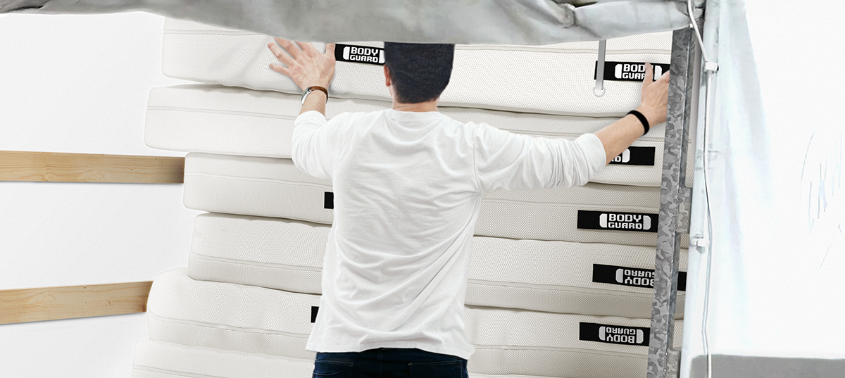 Sustainable mattress donations: A person pushes a mattress onto a pile of mattresses on a covered loading area.