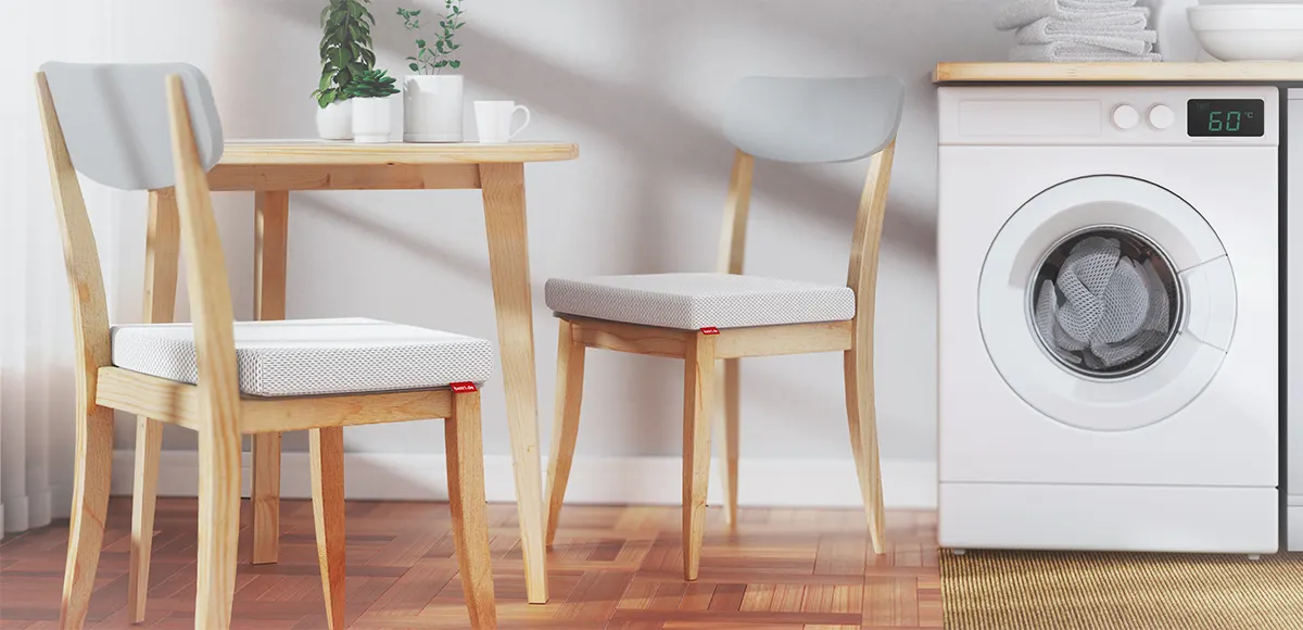 A table with two chairs on which the BODYGUARD® seat cushion is placed. Next to it is a washing machine.