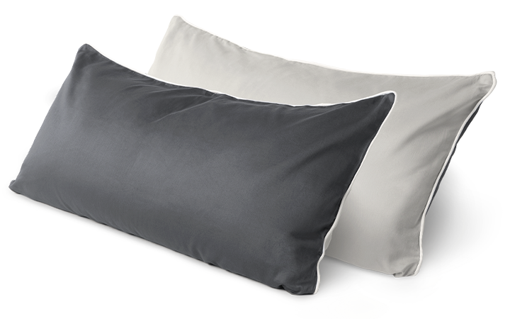 Two BODYGUARD Visco pillows covered with BODYGUARD satin bedding are placed one behind the other. The front pillow (80x40 cm) shows the light-colored side of the cover, the rear pillow shows the dark side.
