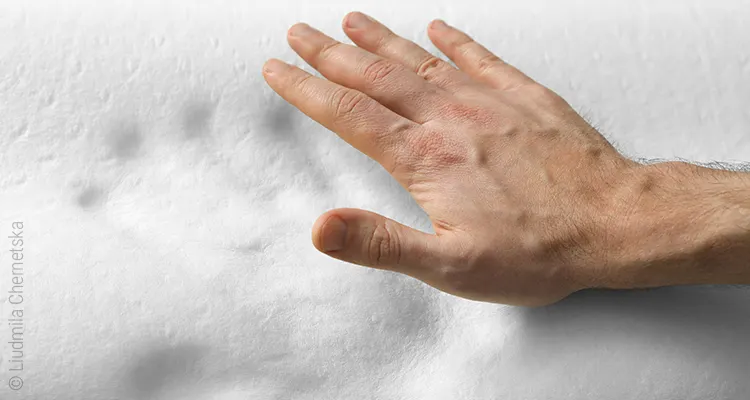 A hand hovers over a foam mattress made of visco foam in which the handprint is still visible