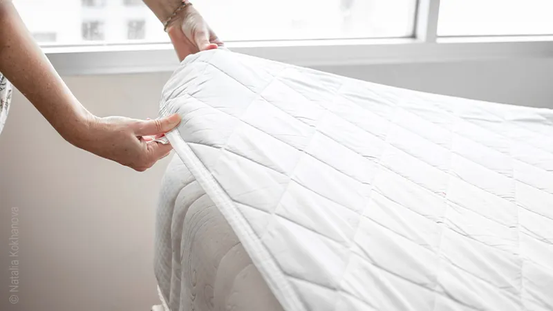 Photo: Two hands pulling the corner of a mattress protector lying on a mattress.