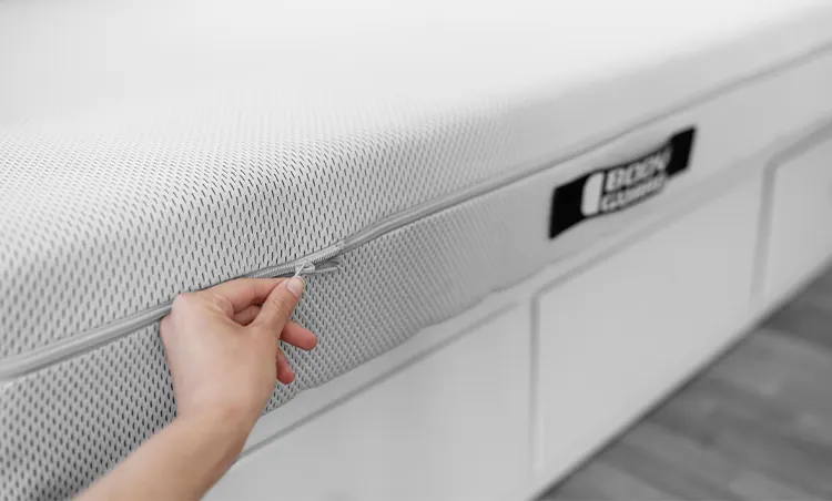 A hand opens the zipper of a BODYGUARD mattress