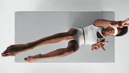 Top view: A person in pyjamas and a sleep mask is lying on a mattress, stretching their arms and legs upwards towards the viewer.