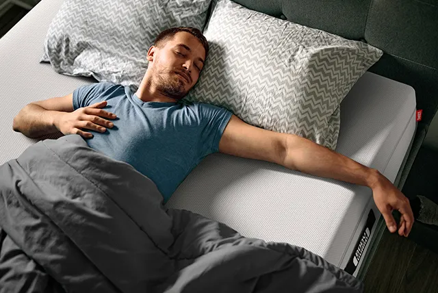 Photo: A person lies on a BODYGUARD mattress with their eyes closed in a bedroom at night.