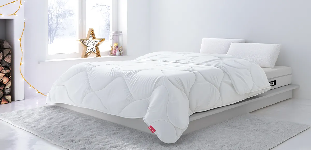 A bright bedroom with winter decorations. A BODYGUARD Winter Duvet 135x200 cm lies on the bed. Snow covers the ground outside the window.