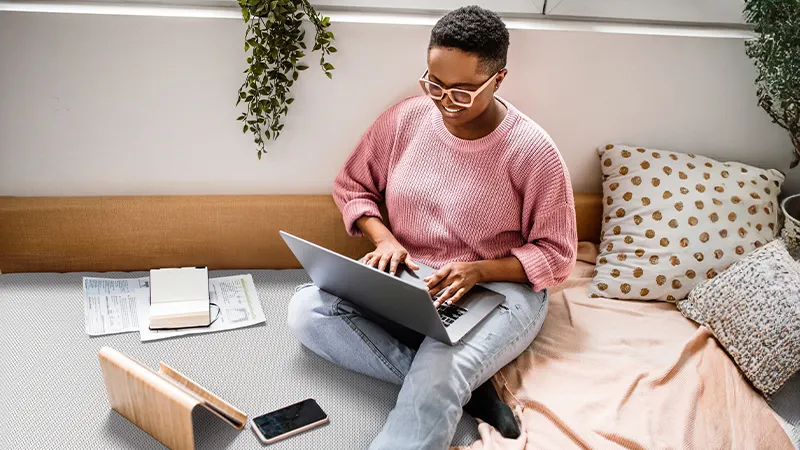 A person is sitting on the floor with an open laptop on their legs. 