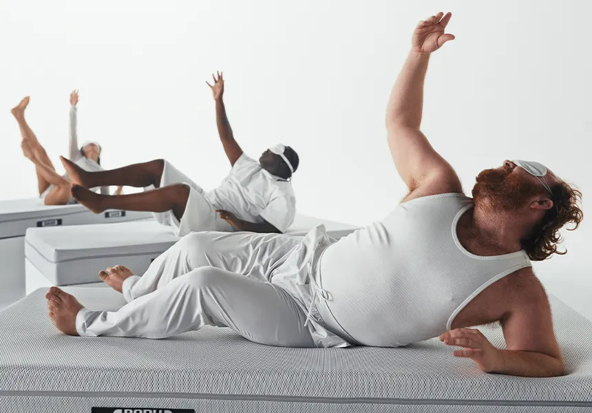 Foto: Standbild von Personen auf bett1 Matratzen, die eine Art liegenden Ausdruckstanz aufführen. Die Personen tragen weiße Schlafkleidung sowie Schlafmasken